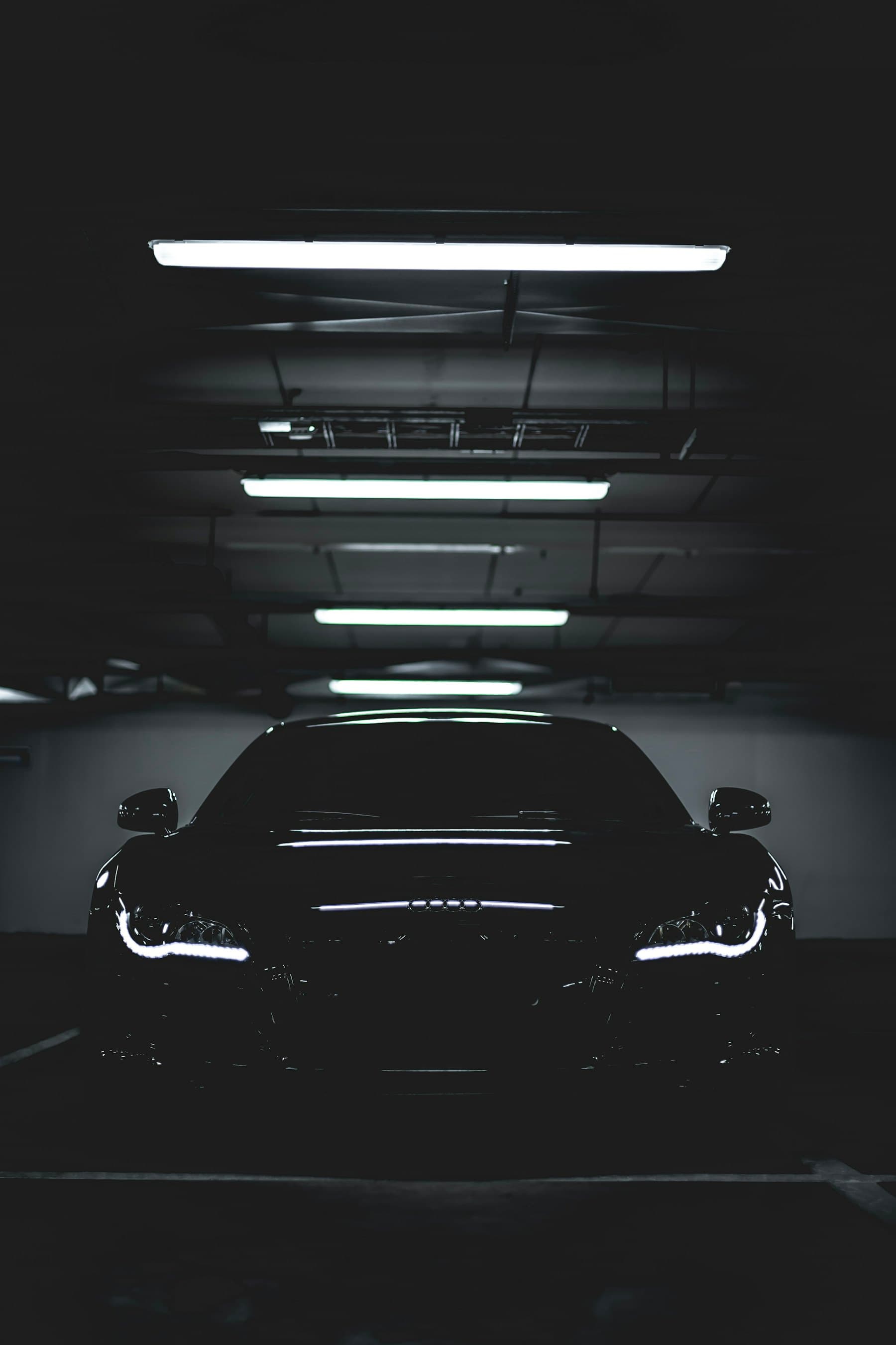 A dark car silhouetted under a row of strip lights in an underground garage