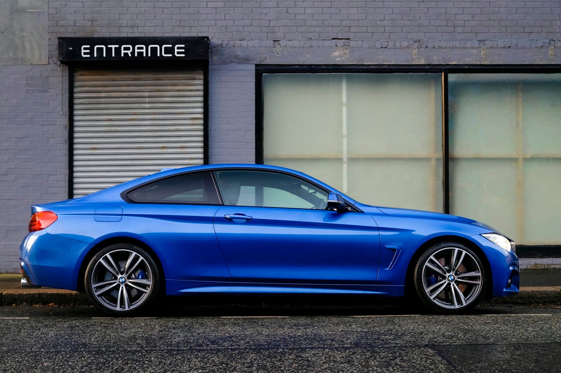Blue BMW 4 Series coupe parked in profile beside a building entrance