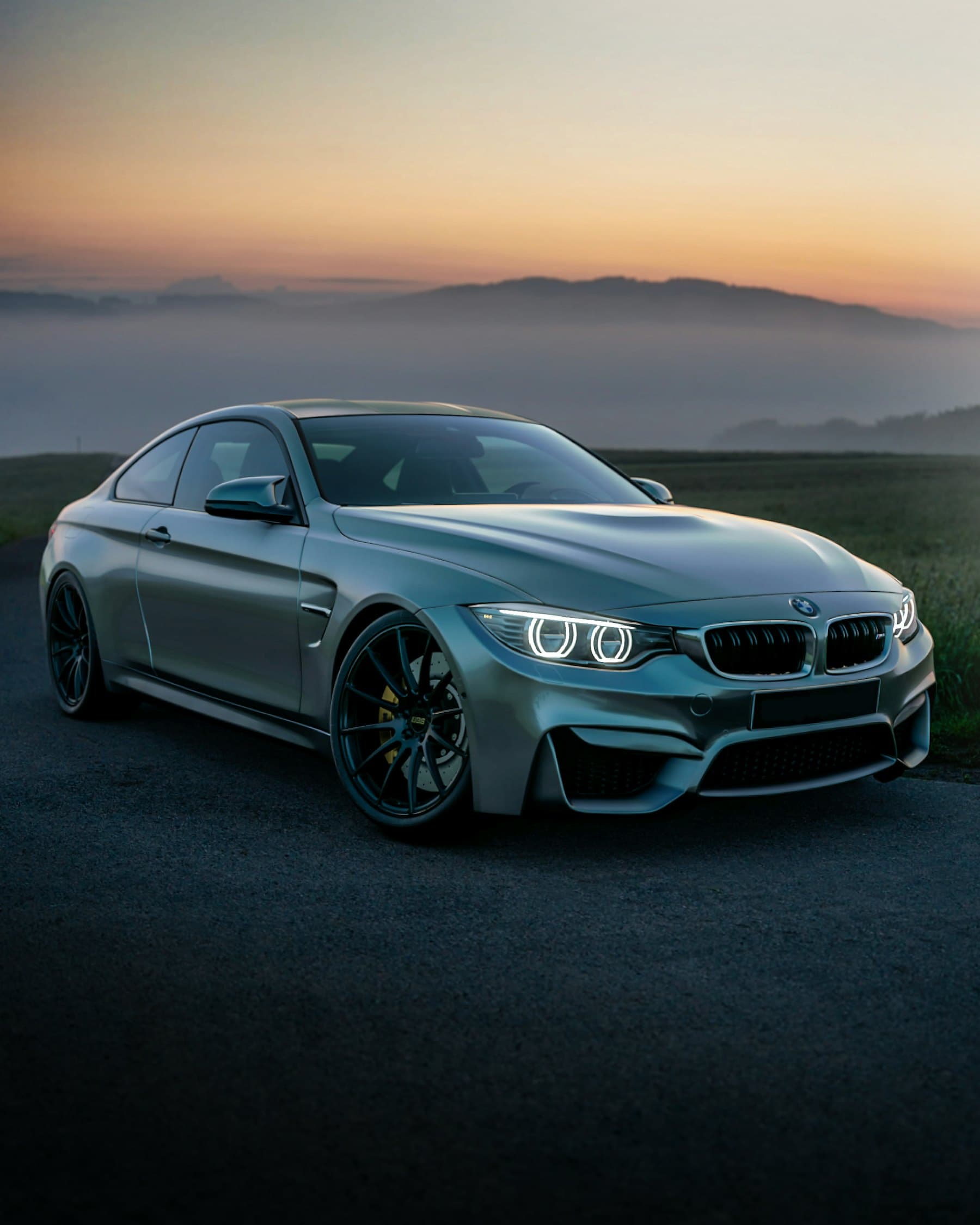 Grey BMW M4 coupe parked on a hillside road at dusk