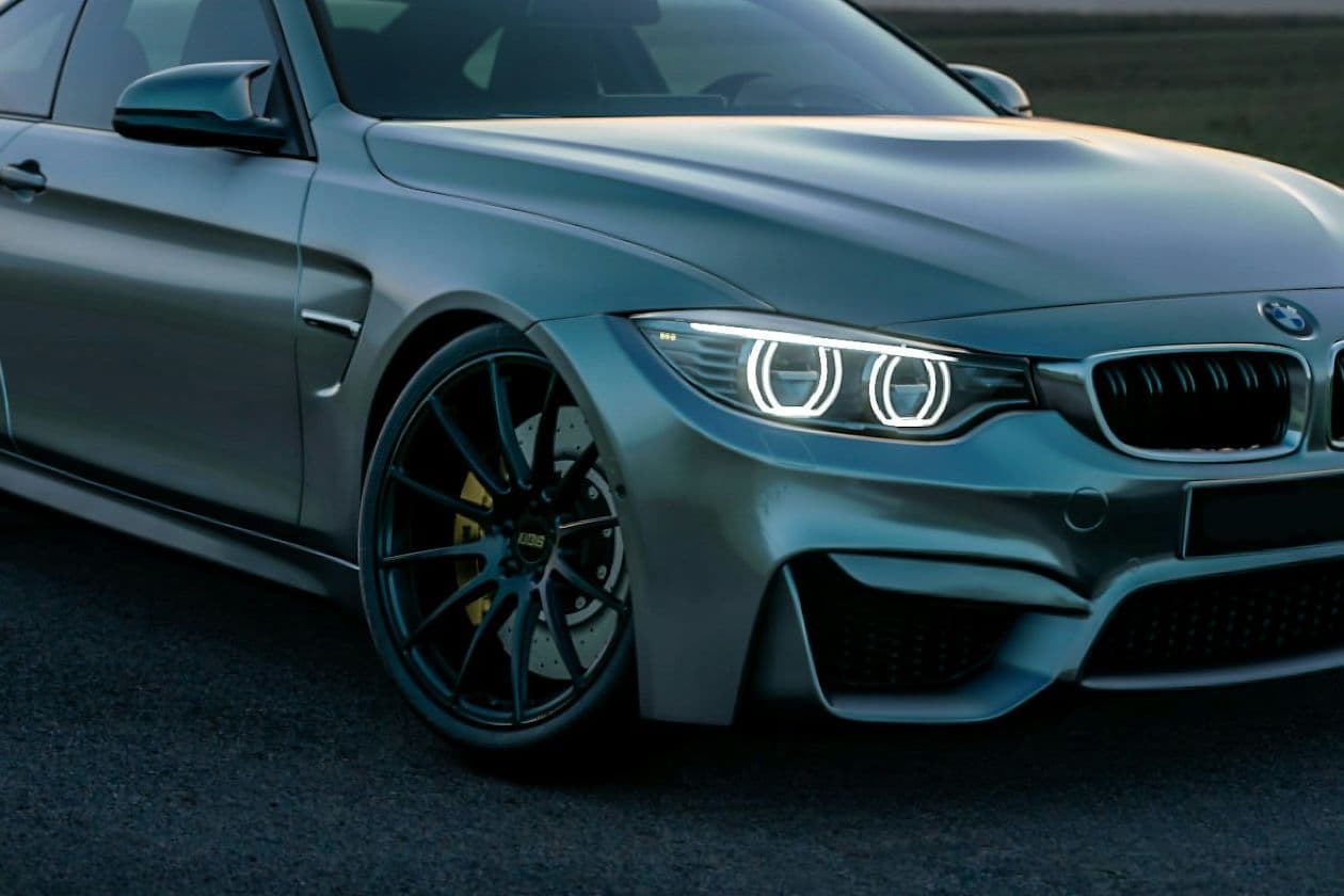Close front three-quarter view of the grey BMW M4 with angel-eye headlights