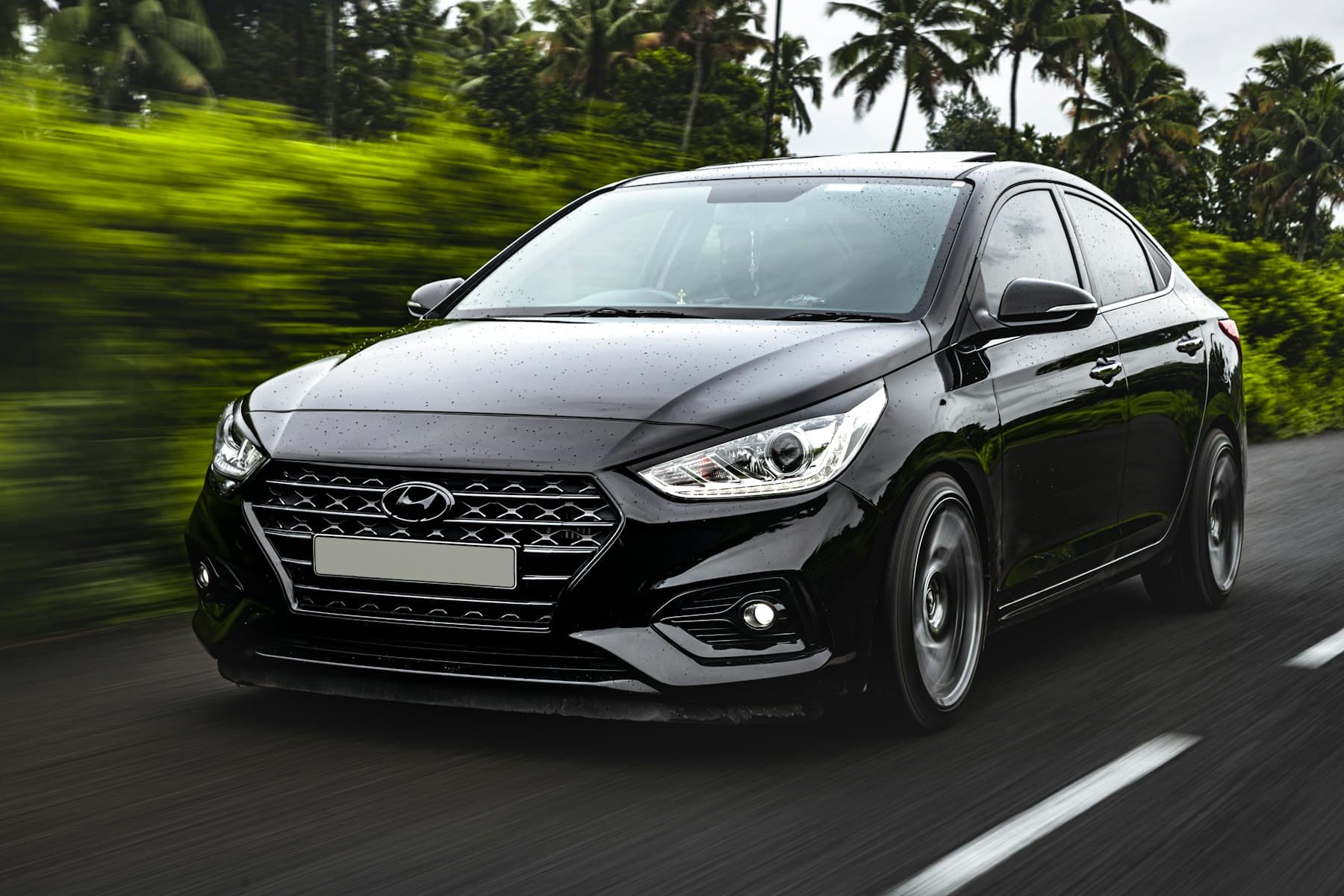 Black Hyundai Accent sedan driving through a tropical landscape