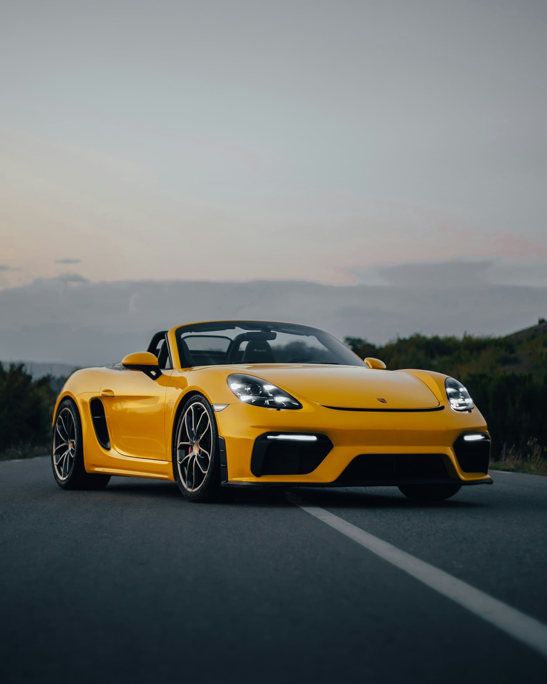 Yellow Porsche 718 Spyder roadster on an empty road at sunset
