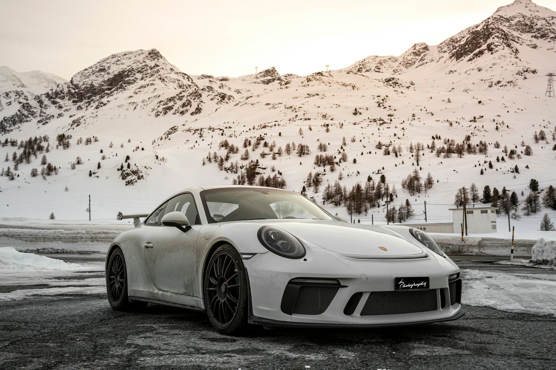 White Porsche 911 GT3 with rear wing parked on a snowy mountain pass