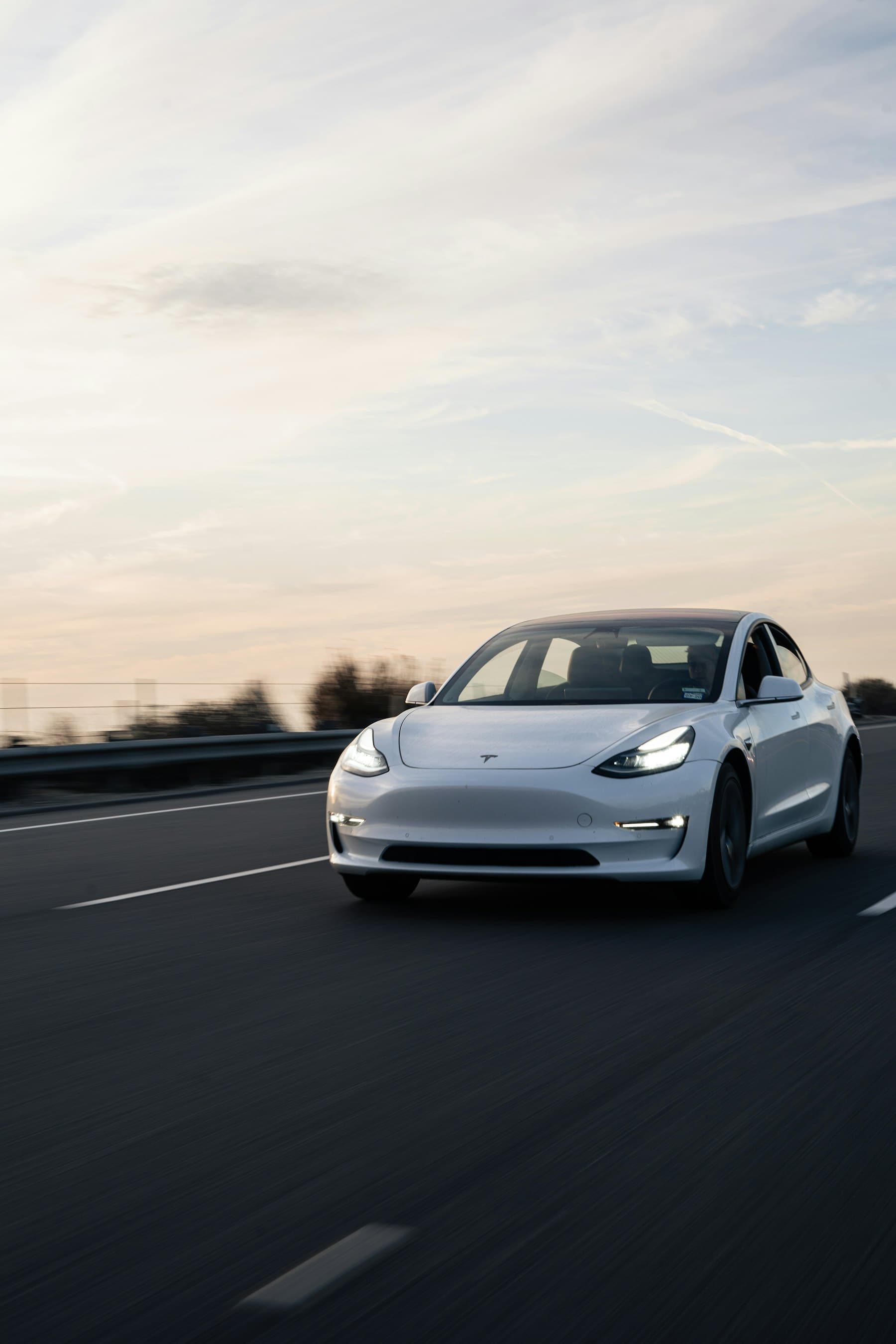 White Tesla Model 3 driving on an open road at dusk